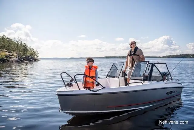 A man and a boy in life jackets on a small boat, surrounded by calm water and trees under a blue sky with clouds.